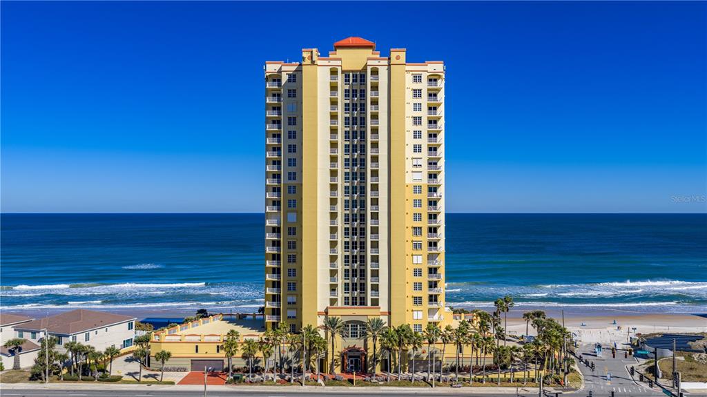 A tall, yellow multi-story condominium building stands directly on a sandy beach by the ocean — 2300 N ATLANTIC AVENUE UNIT 101, DAYTONA BEACH, FL