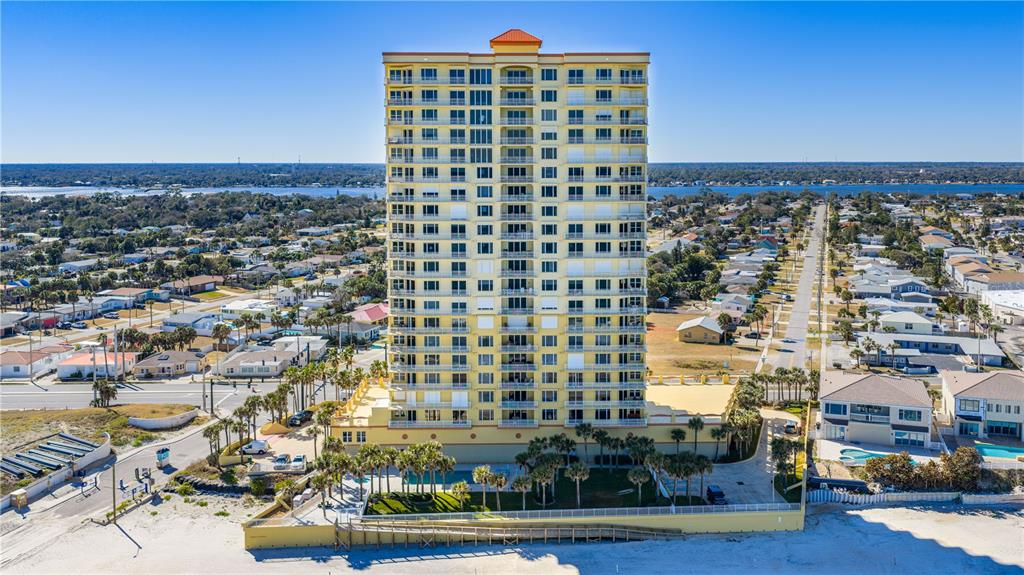 An aerial view of a tall, yellow beachfront condominium building surrounded by a residential neighborhood — 2300 N ATLANTIC AVENUE UNIT 101, DAYTONA BEACH, FL