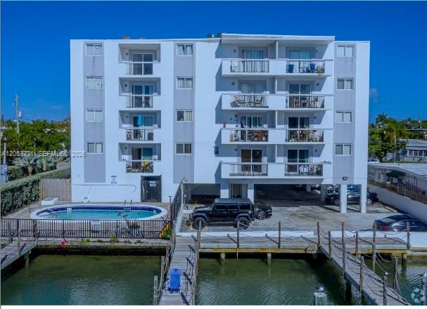 A multi-story apartment building with balconies stands beside a swimming pool and a wooden dock — 8101 Crespi Blvd # 404, Miami Beach FL 33141, MIAMI BEACH, FL