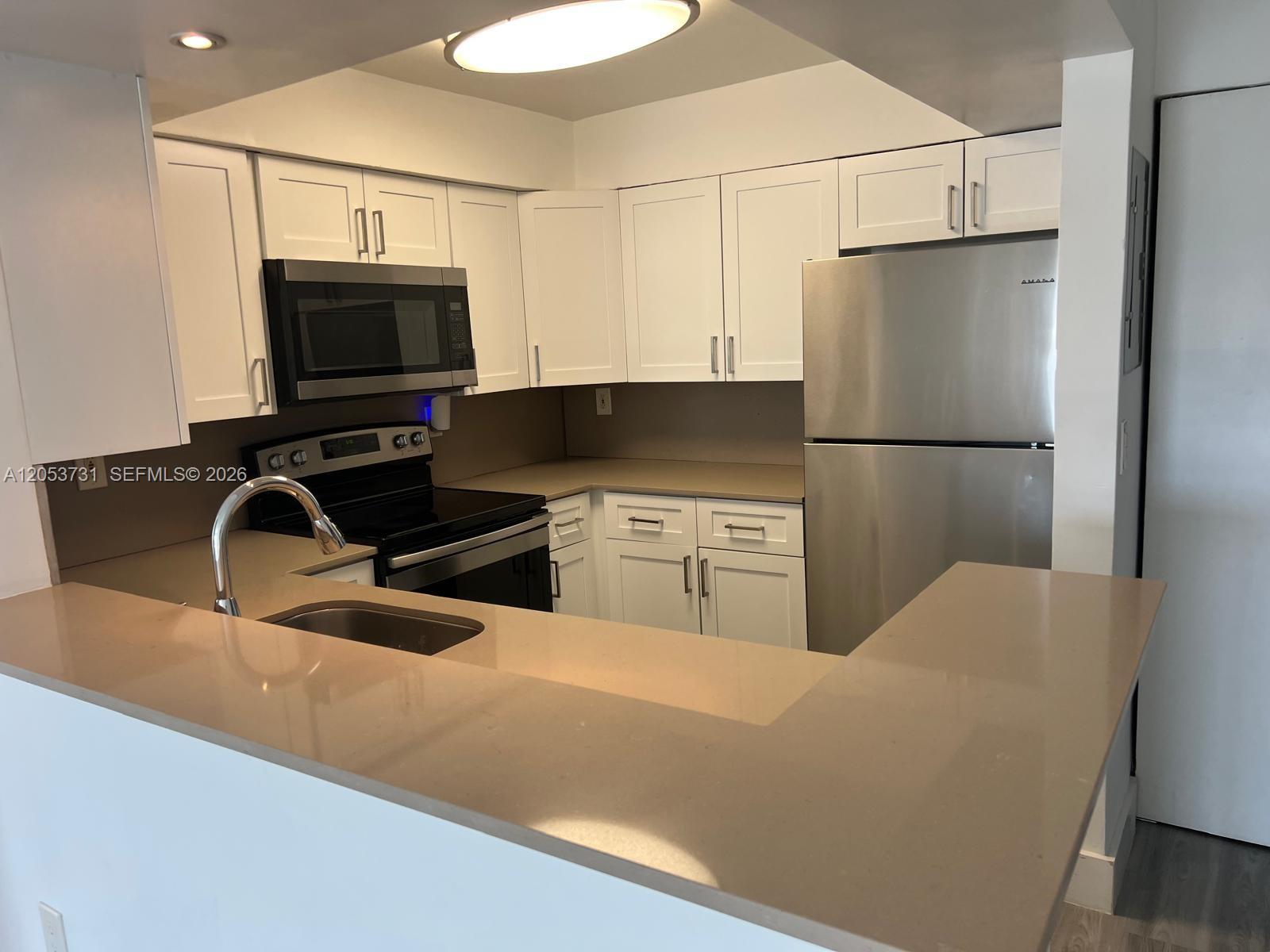 A kitchen features white cabinets, stainless steel appliances, and tan countertops with a breakfast bar — 8101 Crespi Blvd # 404, Miami Beach FL 33141, MIAMI BEACH, FL