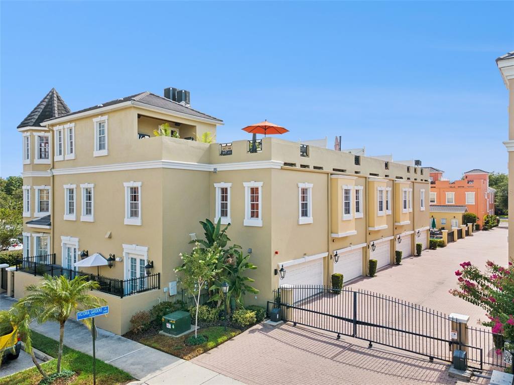 An exterior view of a multi-story tan townhouse complex with a gated driveway and rooftop terrace — 2402 VICTORIA GARDENS LANE, TAMPA, FL