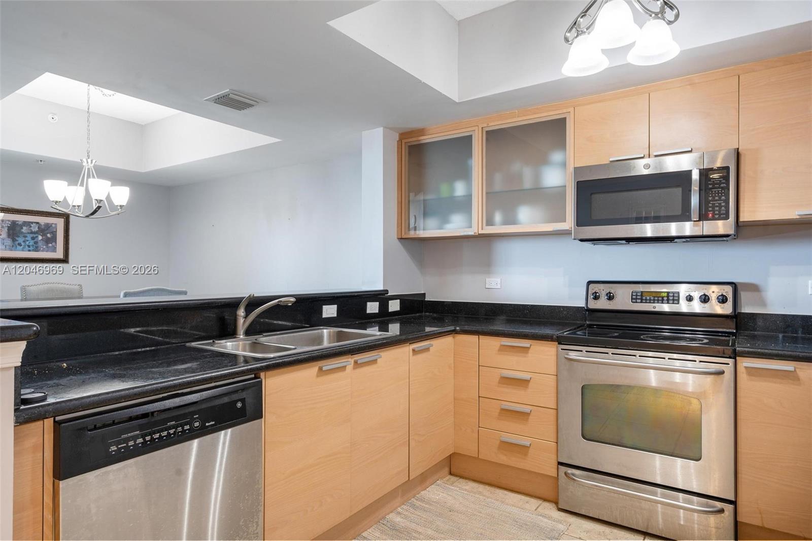 A kitchen features light wood cabinets, black countertops, stainless steel appliances, and a breakfast bar — 140 S Dixie Hwy # 609, Hollywood FL 33020, HOLLYWOOD, FL
