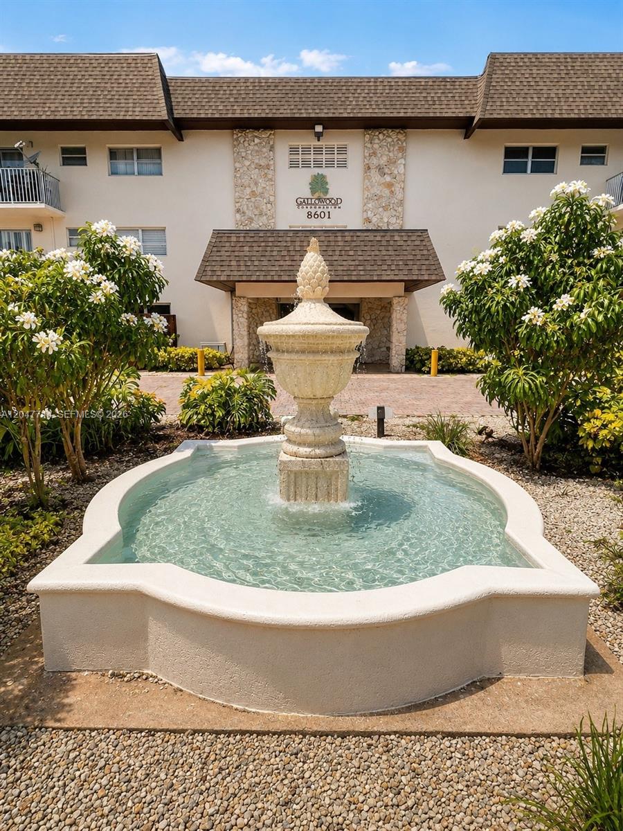 A stone fountain sits in front of a multi-story condominium building with a brown roof — 8601 SW 94th St # 105W, Miami FL 33156, MIAMI, FL