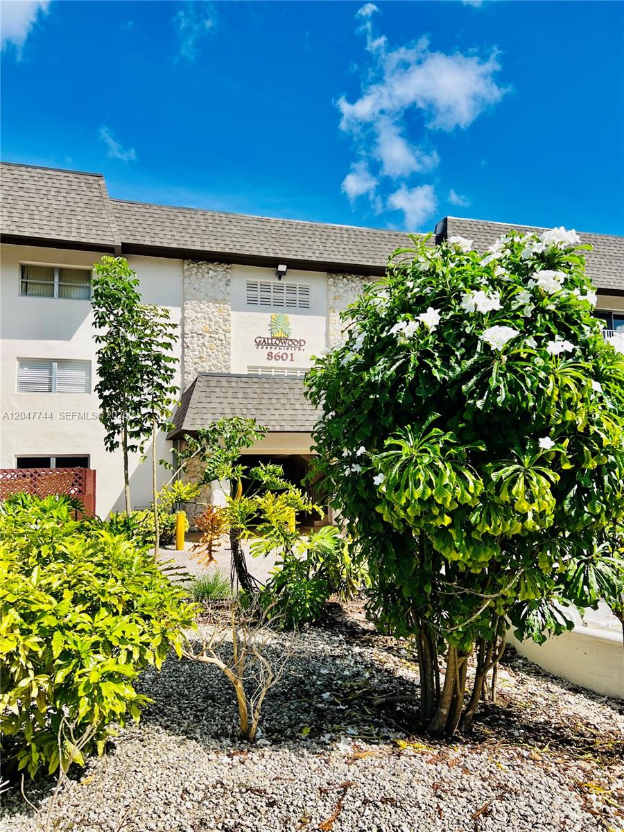 The exterior of a multi-story condominium building features a stone facade and lush landscaping — 8601 SW 94th St # 105W, Miami FL 33156, MIAMI, FL