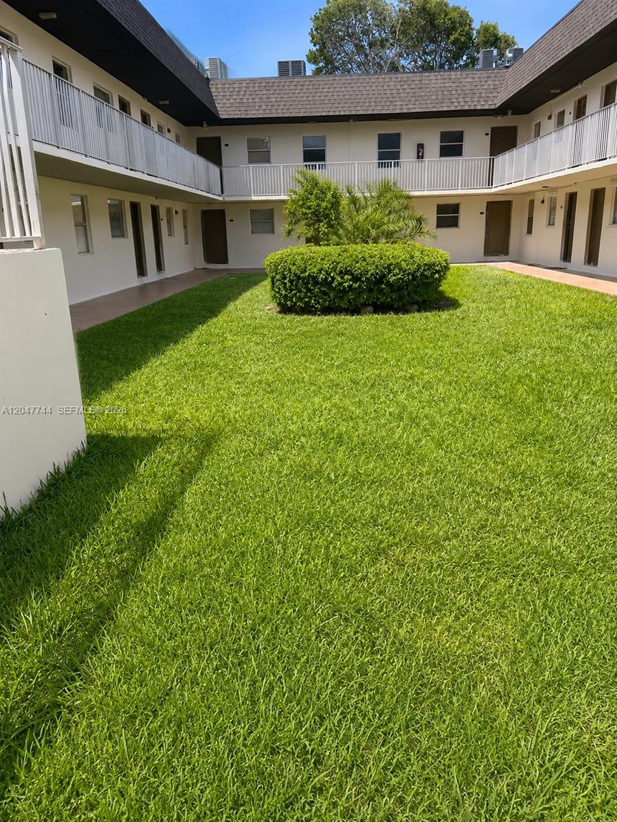 A courtyard with a green lawn and a central bush surrounded by two-story apartment buildings — 8601 SW 94th St # 105W, Miami FL 33156, MIAMI, FL