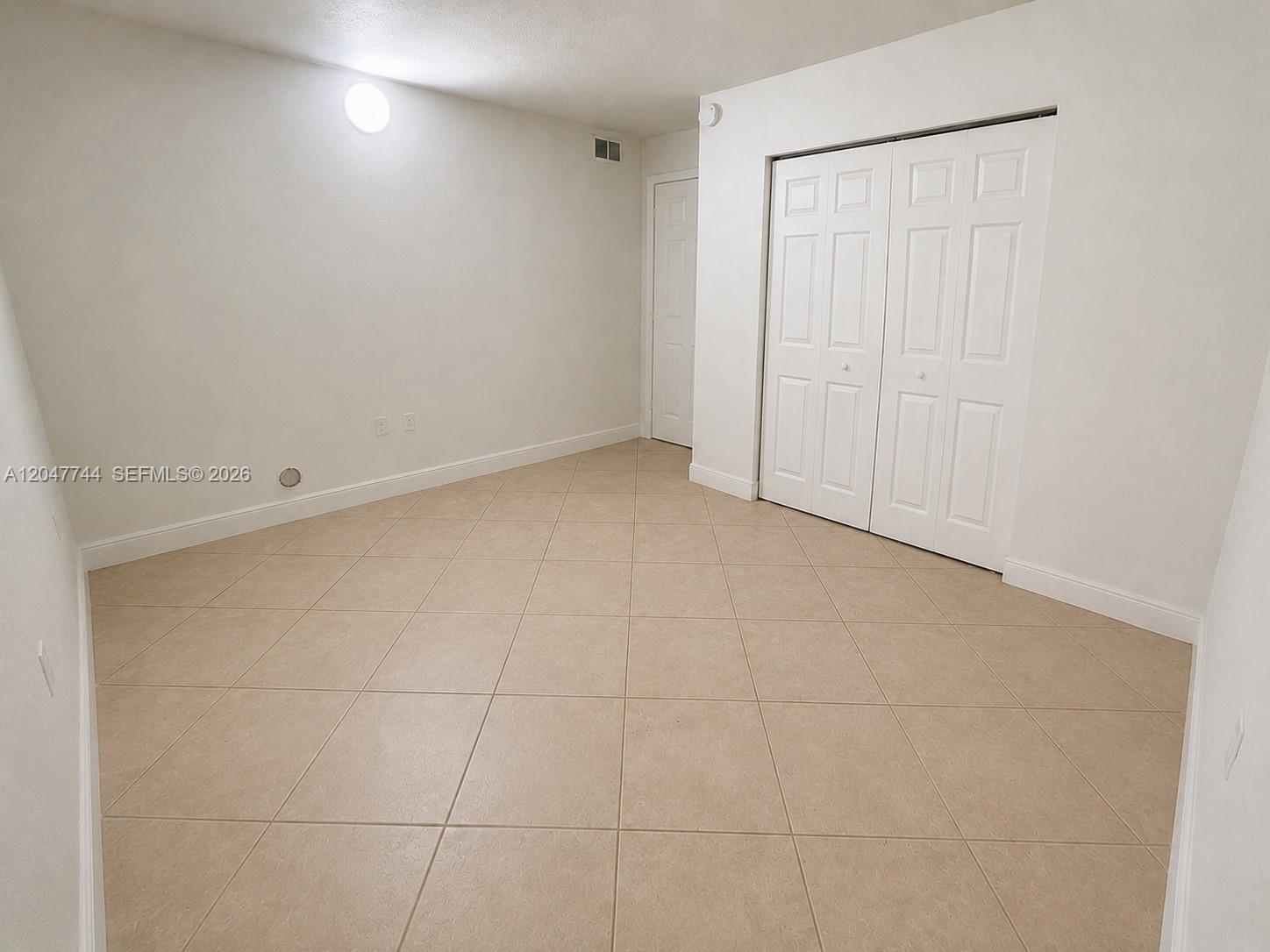 An empty room features white walls, beige tile flooring, and a white bi-fold closet door — 8601 SW 94th St # 105W, Miami FL 33156, MIAMI, FL