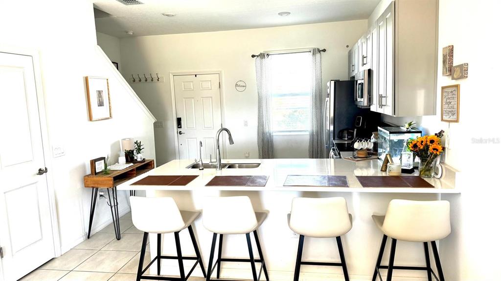 A kitchen features a white island with four bar stools, light cabinetry, and stainless appliances — 3322 COMPOSITION STREET, KISSIMMEE, FL