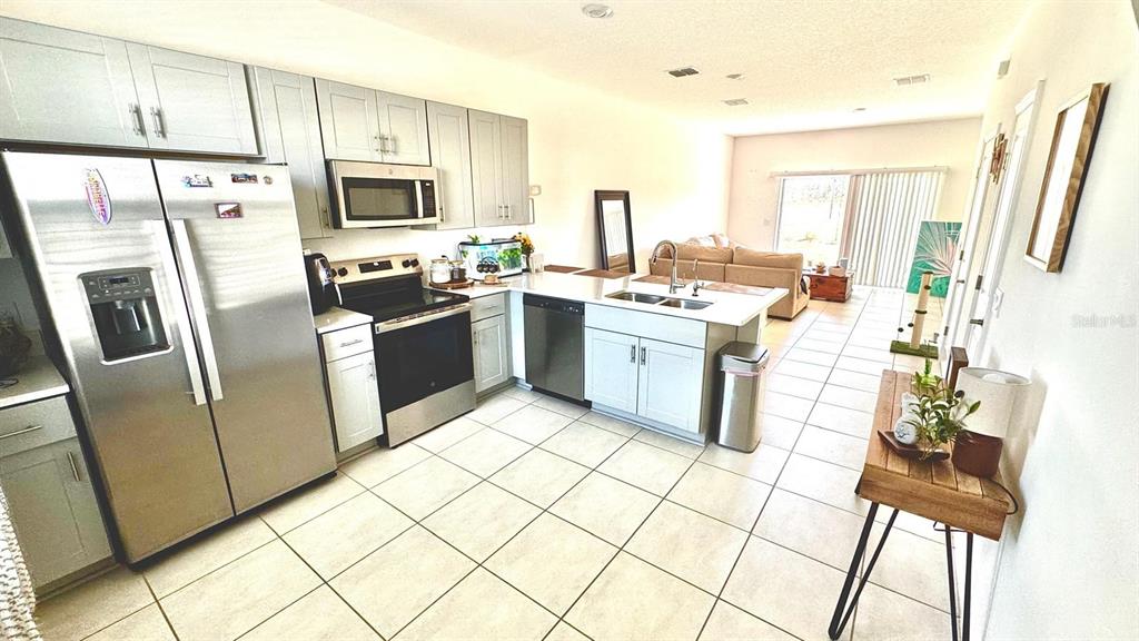 A kitchen with light gray cabinets, stainless steel appliances, and tile flooring opens to a living area — 3322 COMPOSITION STREET, KISSIMMEE, FL