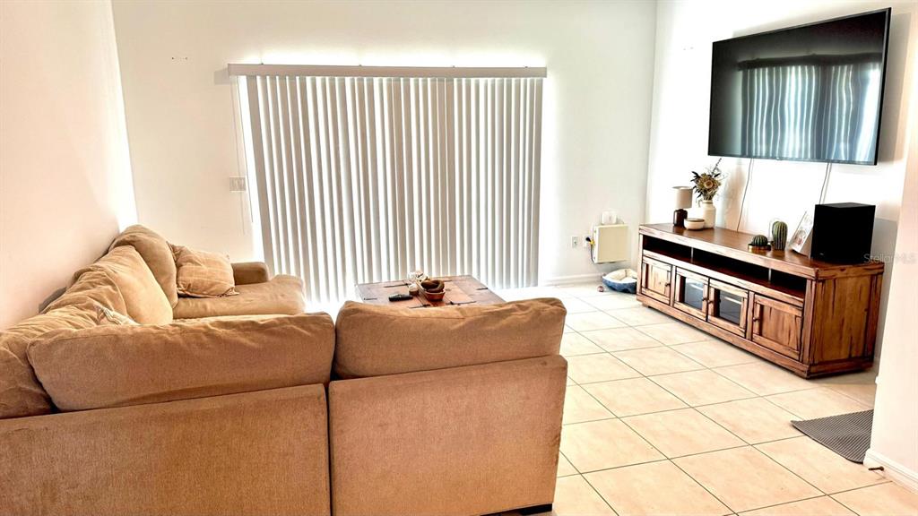 A living room features a tan sectional sofa, a wooden media console, and vertical blinds — 3322 COMPOSITION STREET, KISSIMMEE, FL