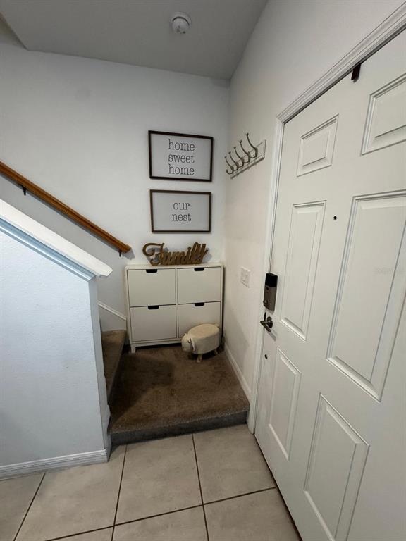 An entryway features a white shoe cabinet, wall decor, a staircase, and a white door — 3322 COMPOSITION STREET, KISSIMMEE, FL