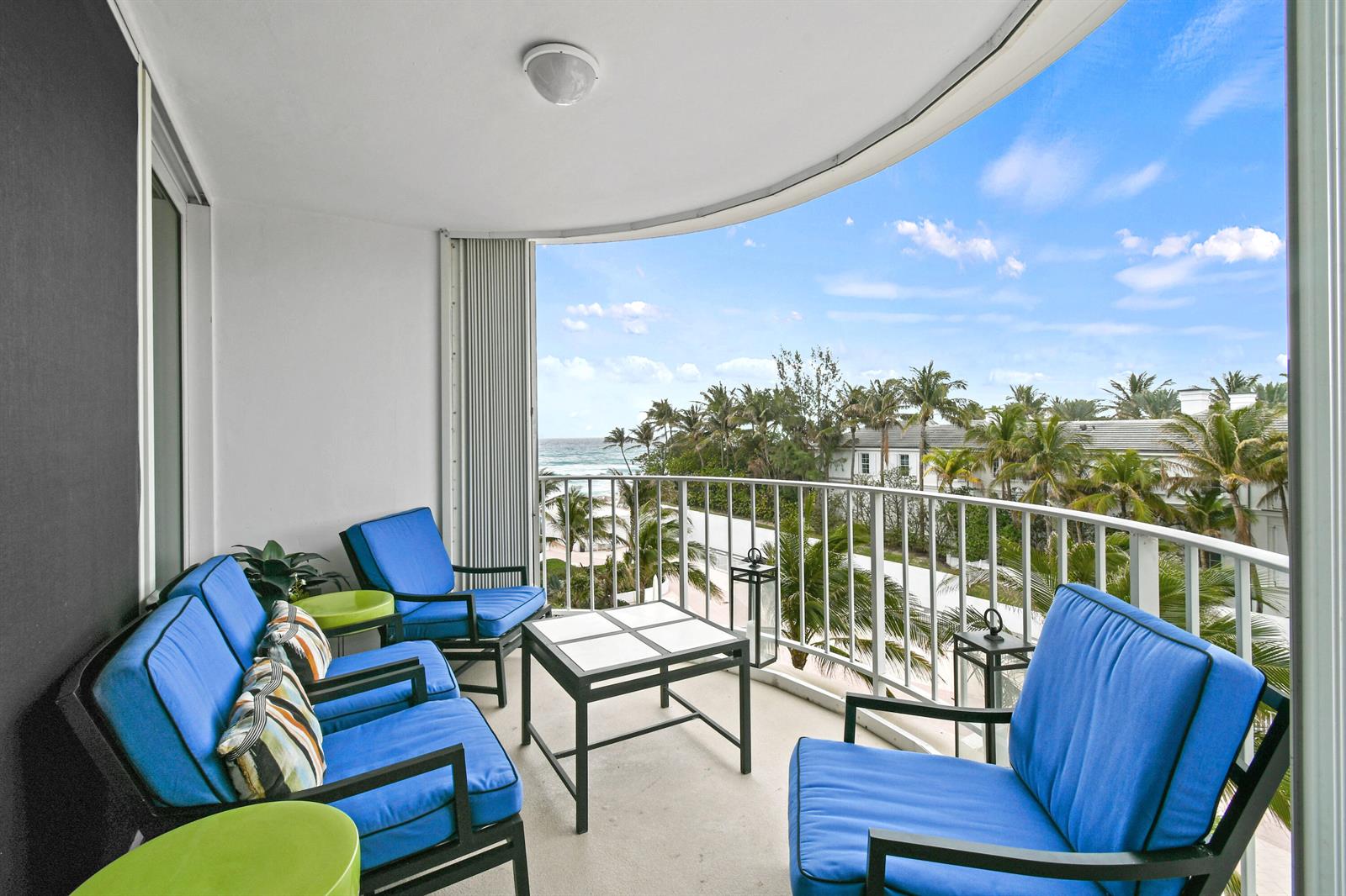 A balcony with blue cushioned chairs and a table overlooks a beach and palm trees — 2295 S Ocean Boulevard # 505, Palm Beach FL 33480, PALM BEACH, FL