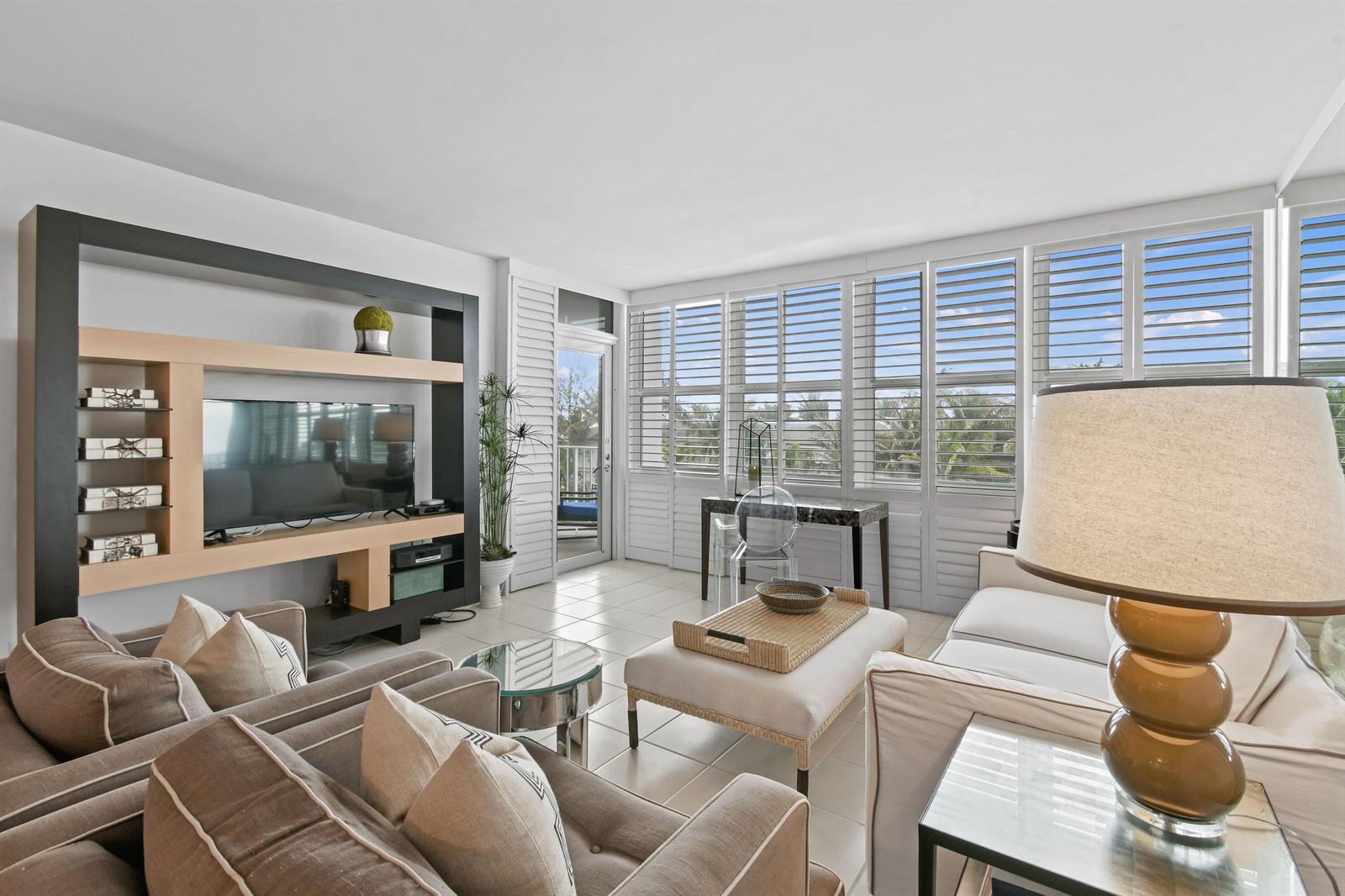 A living room features tile floors, a large media console, and plantation shutters over windows — 2295 S Ocean Boulevard # 505, Palm Beach FL 33480, PALM BEACH, FL