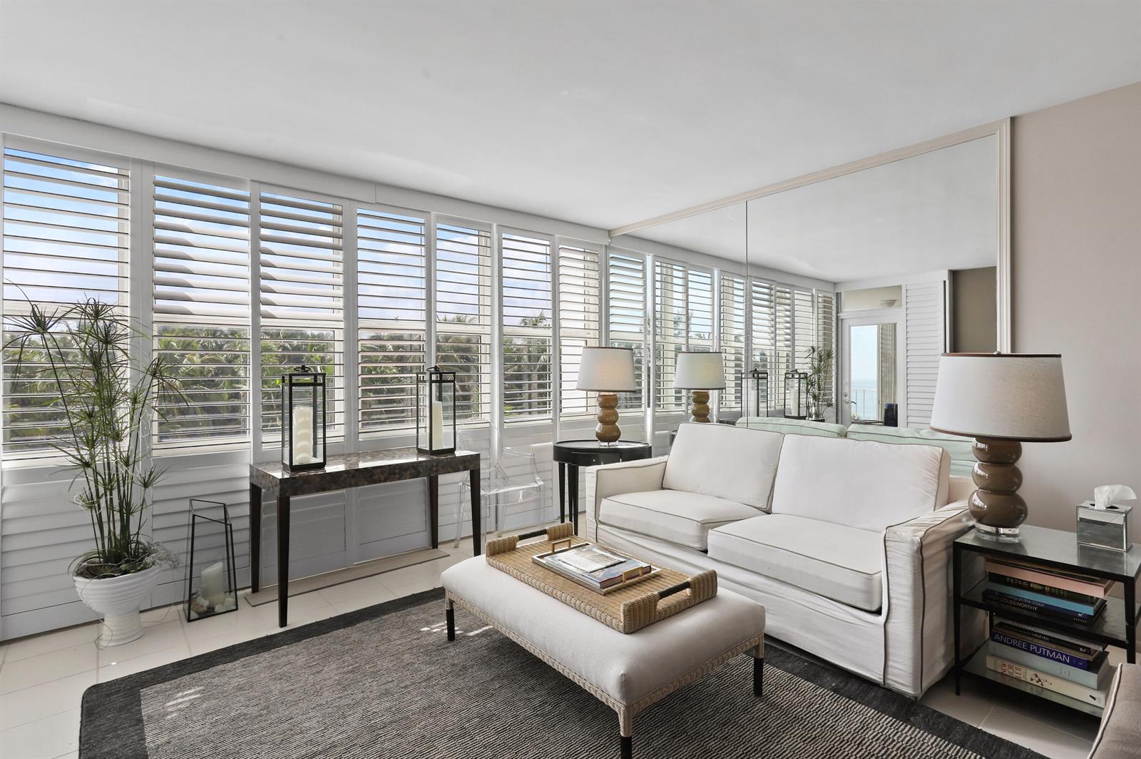 A bright living room features white sofas, a dark area rug, and floor-to-ceiling plantation shutters — 2295 S Ocean Boulevard # 505, Palm Beach FL 33480, PALM BEACH, FL