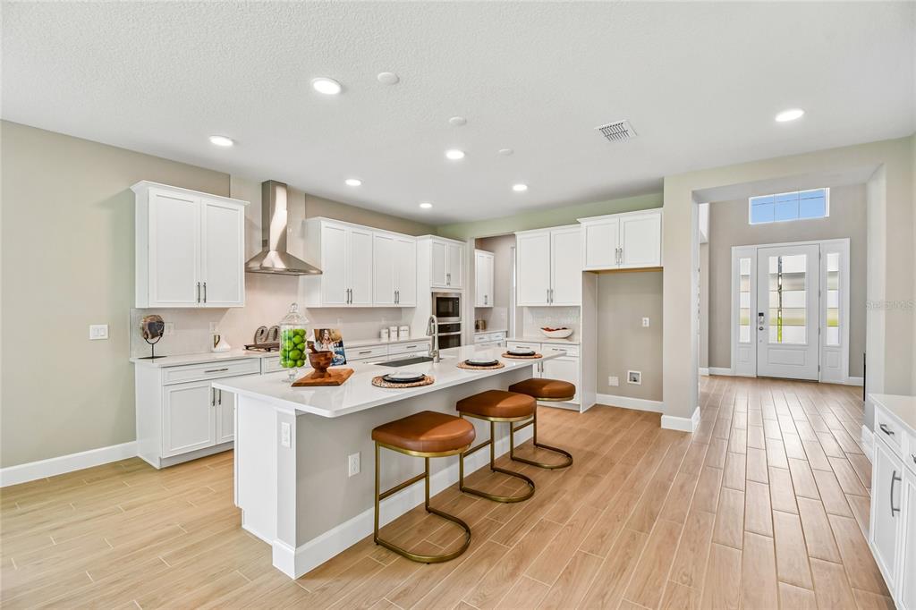 A modern kitchen features white cabinetry, a central island with bar stools, and wood-look flooring — 3318 WOLF LAKE AVENUE, APOPKA, FL