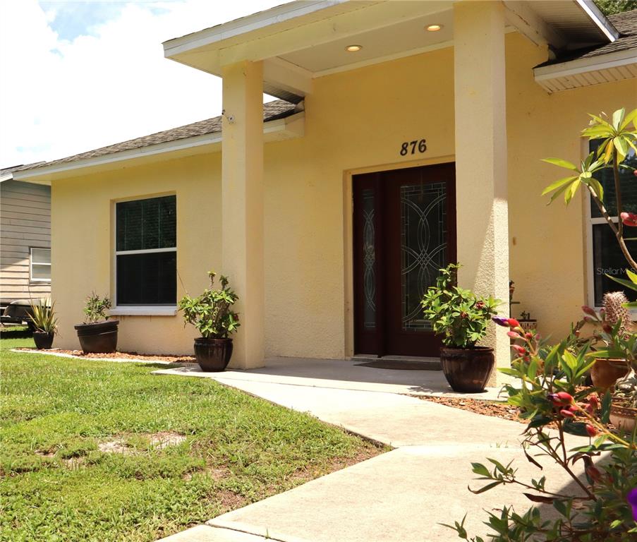 A yellow house exterior features a covered entryway with columns and a decorative front door — 876 CR 467, LAKE PANASOFFKEE, FL