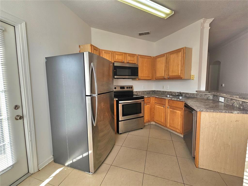 A kitchen features stainless steel appliances, light wood cabinets, and tan tile flooring — 18058 VILLA CREEK DRIVE UNIT 18058, TAMPA, FL