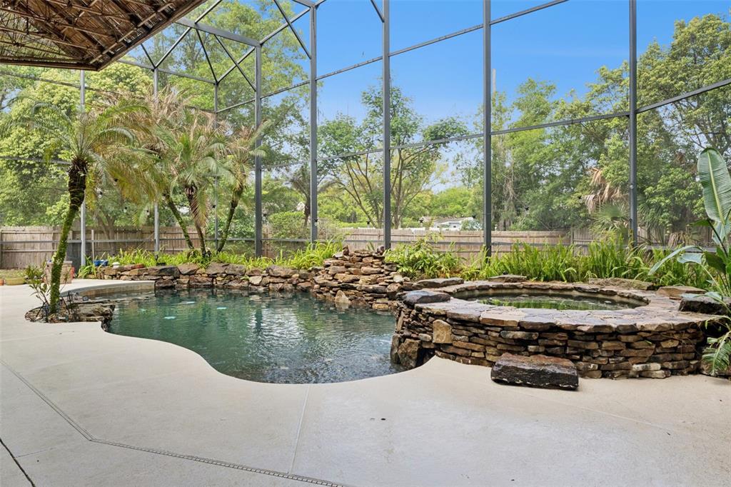 A screened-in pool area features a rock waterfall, a stone hot tub, and palm trees — 216 JUNIPER RIDGE COURT, SANFORD, FL