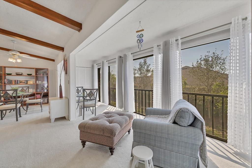 A living area with a tufted ottoman, armchair, dining set, and large windows overlooking trees — 2446 CLUBHOUSE CIRCLE UNIT 202, SARASOTA, FL