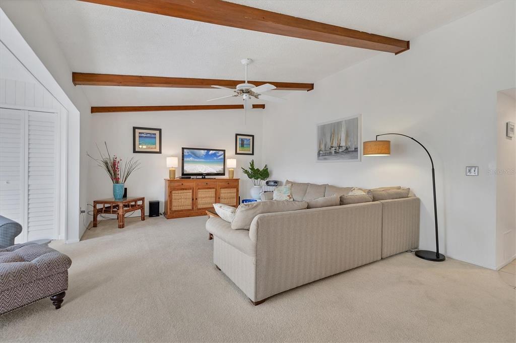 A living room features a beige sectional sofa, wood ceiling beams, and a television console — 2446 CLUBHOUSE CIRCLE UNIT 202, SARASOTA, FL