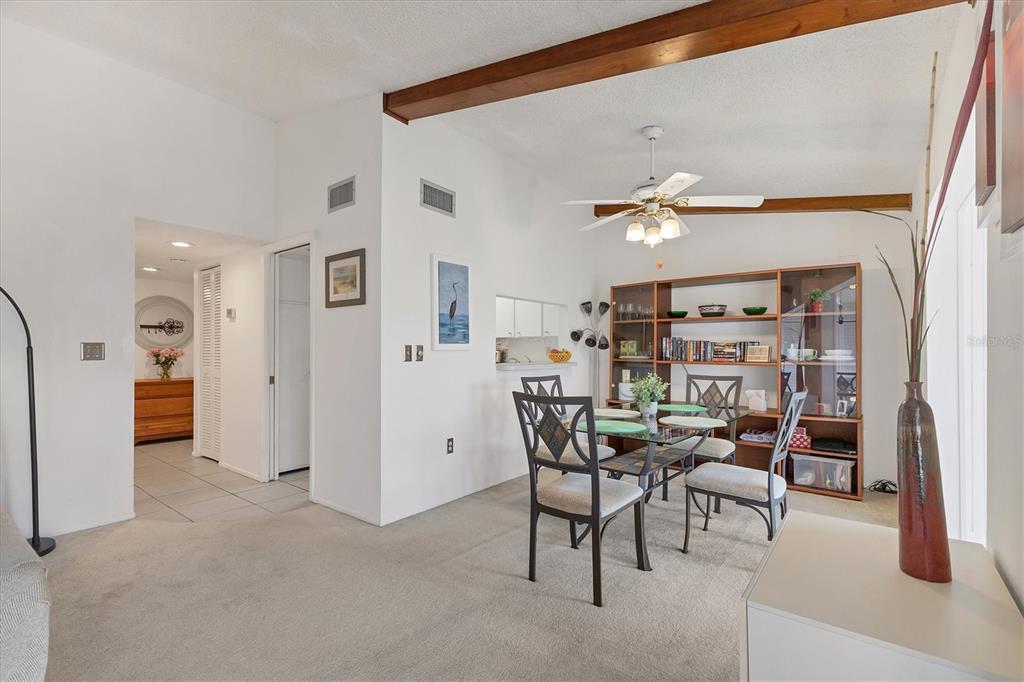 A dining area features a glass table, metal chairs, a wooden bookshelf, and exposed beams — 2446 CLUBHOUSE CIRCLE UNIT 202, SARASOTA, FL