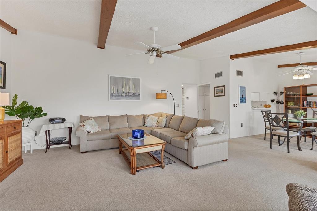 A living room with a beige sectional sofa, wood-beamed ceilings, and an adjacent dining area — 2446 CLUBHOUSE CIRCLE UNIT 202, SARASOTA, FL