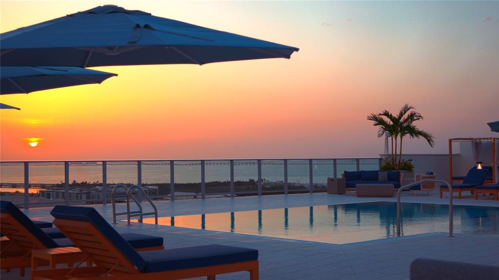 A rooftop swimming pool with lounge chairs and umbrellas overlooks the ocean at sunset — 5713 BOWEN DANIEL DR. UNIT 1603, TAMPA, FL