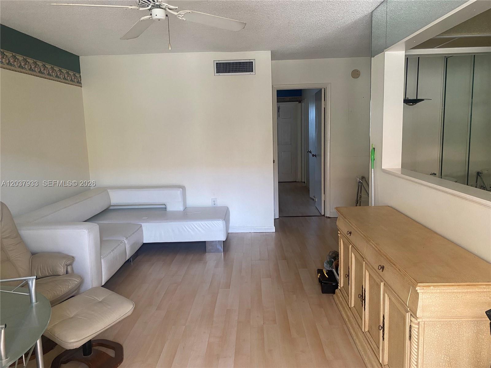 A living room features a white sectional sofa, a wooden cabinet, and light wood flooring — 415 NE 2nd St # 222, Hallandale Beach FL 33009, HALLANDALE BEACH, FL
