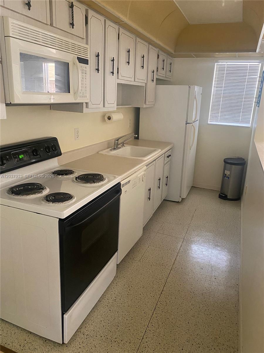 A galley-style kitchen features white cabinets, white appliances, and light-colored countertops — 415 NE 2nd St # 222, Hallandale Beach FL 33009, HALLANDALE BEACH, FL