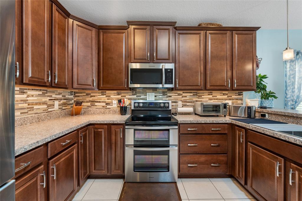 A kitchen features dark wood cabinets, stainless steel appliances, and a mosaic tile backsplash — 10226 LENOX STREET, CLERMONT, FL