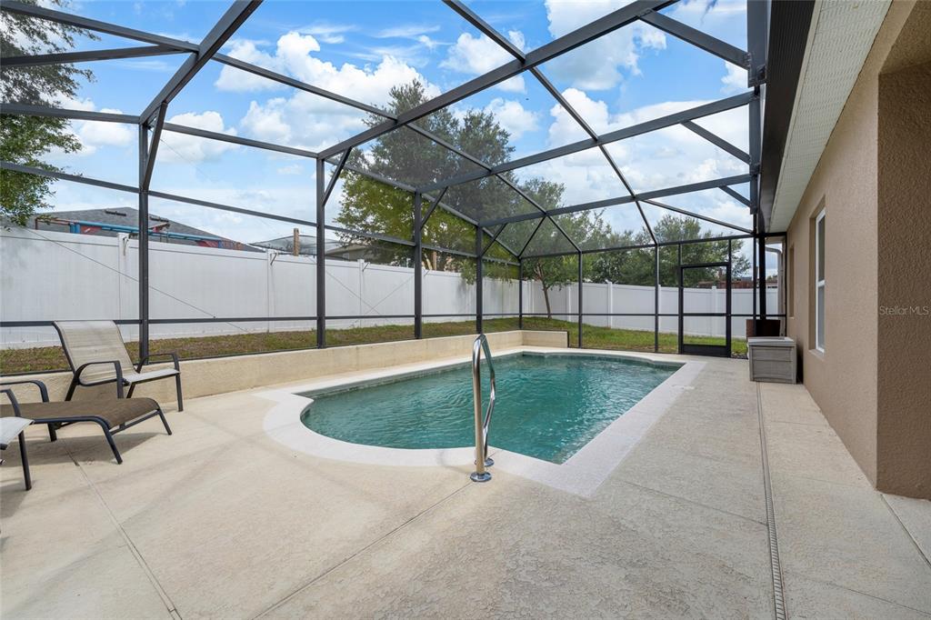 A screened-in patio features a rectangular swimming pool with a metal handrail and lounge chairs — 10226 LENOX STREET, CLERMONT, FL