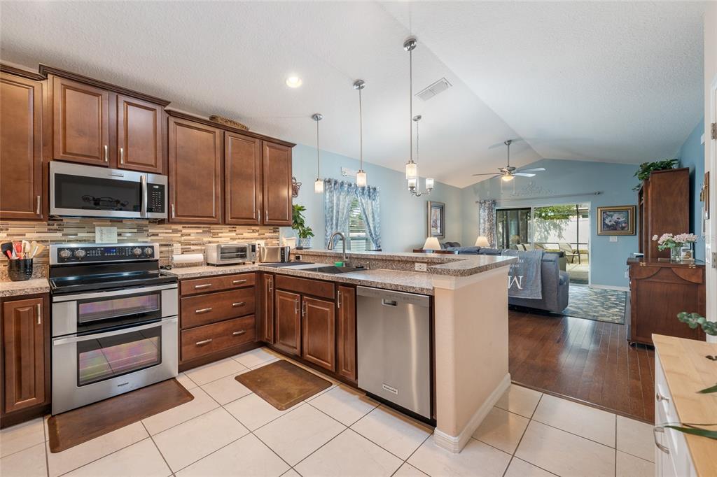A kitchen with dark wood cabinets, stainless steel appliances, and tile flooring opens to a living area — 10226 LENOX STREET, CLERMONT, FL