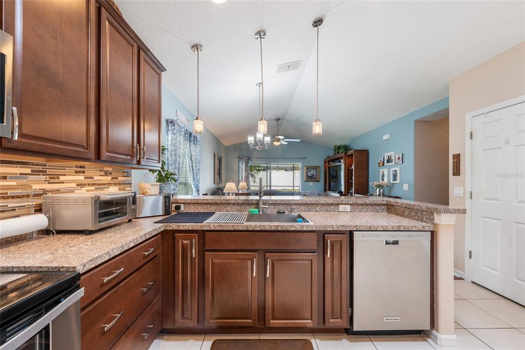 A kitchen with dark wood cabinets, granite countertops, and stainless steel appliances overlooks a living area — 10226 LENOX STREET, CLERMONT, FL