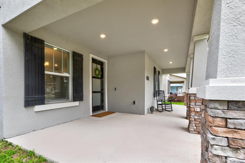 A covered front porch features a glass-paneled door, a rocking chair, and stone-accented columns — 7542 SUMMERLAKE GROVES STREET, WINTER GARDEN, FL