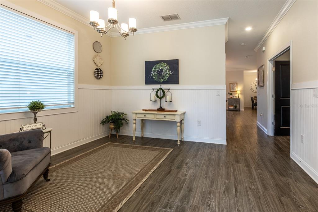 A room with wood-look flooring, white wainscoting, a console table, and a grey armchair — 7542 SUMMERLAKE GROVES STREET, WINTER GARDEN, FL