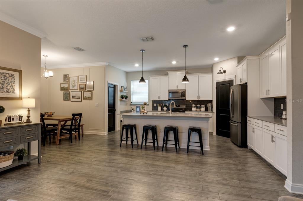 A kitchen with white cabinets, a central island with four stools, and adjacent dining area — 7542 SUMMERLAKE GROVES STREET, WINTER GARDEN, FL
