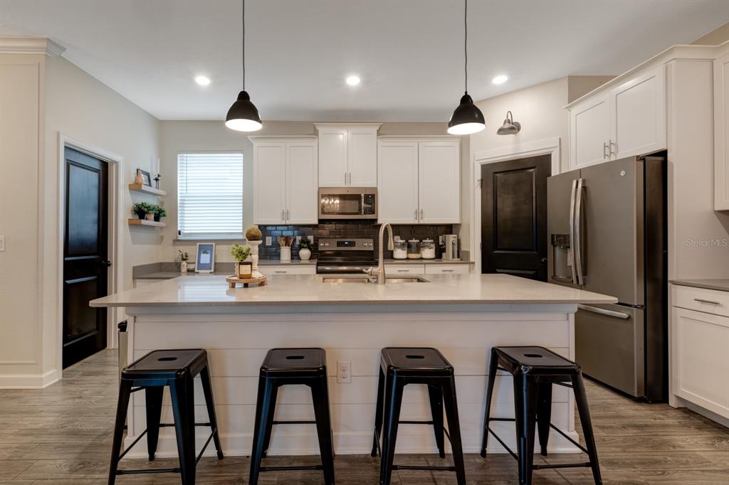 A kitchen features white cabinets, a large island with black stools, and stainless steel appliances — 7542 SUMMERLAKE GROVES STREET, WINTER GARDEN, FL