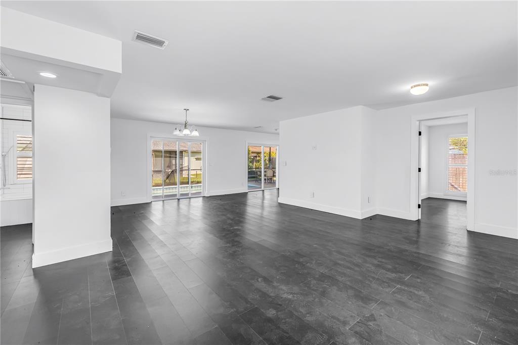 A spacious, open-concept living area features dark wood-look flooring, white walls, and sliding glass doors — 3216 PINE HAVEN DRIVE, CLEARWATER, FL