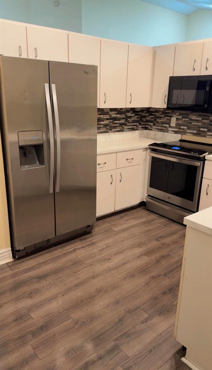 A kitchen featuring white cabinets, stainless steel appliances, a tiled backsplash, and wood-look flooring — 7640 Forest Green Ln, Boynton Beach FL 33436, BOYNTON BEACH, FL