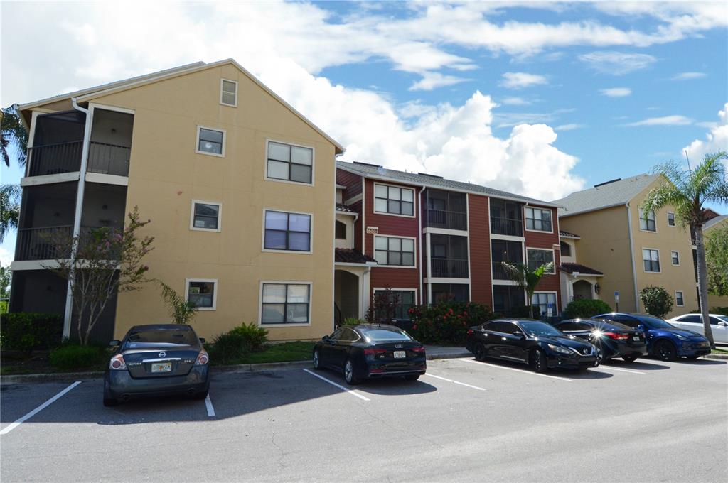 A multi-story apartment building with tan and red siding sits behind a parking lot — 11901 4TH STREET N UNIT 6106, ST PETERSBURG, FL