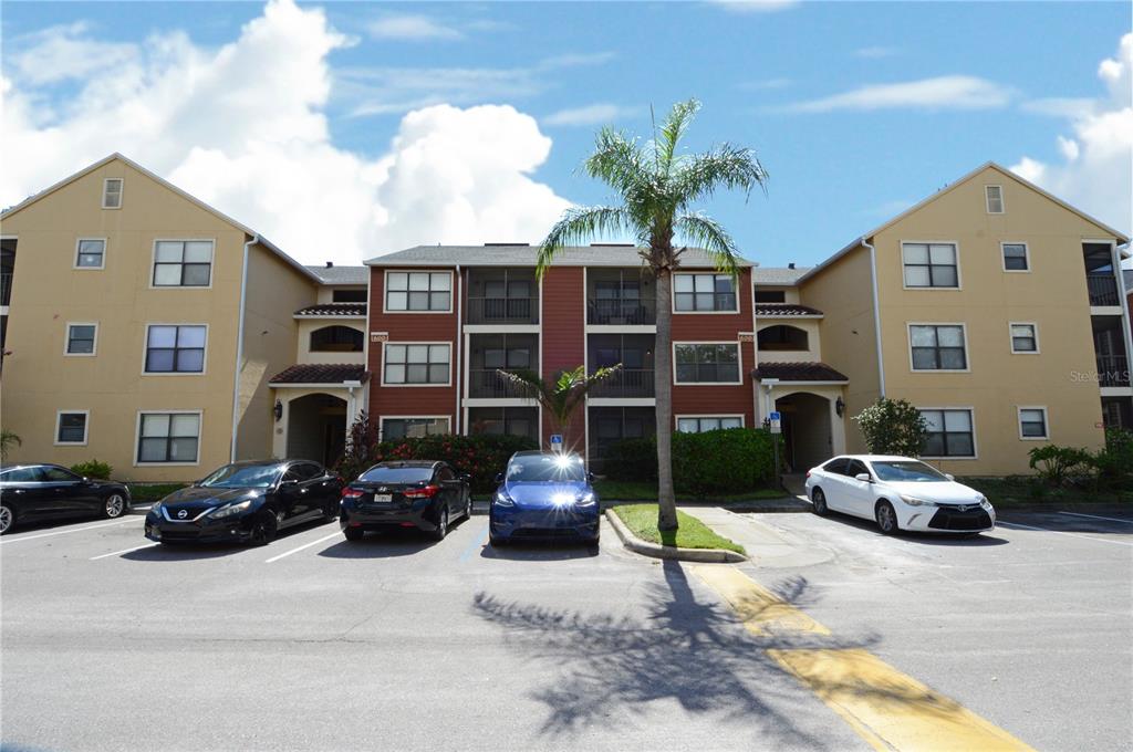 A three-story apartment building with tan and red siding stands behind a parking lot — 11901 4TH STREET N UNIT 6106, ST PETERSBURG, FL