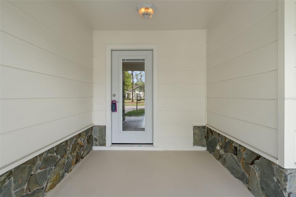 A covered front porch features light-colored horizontal siding, stone veneer accents, and a glass-paneled door — 2224 MERION COURT, SPRING HILL, FL