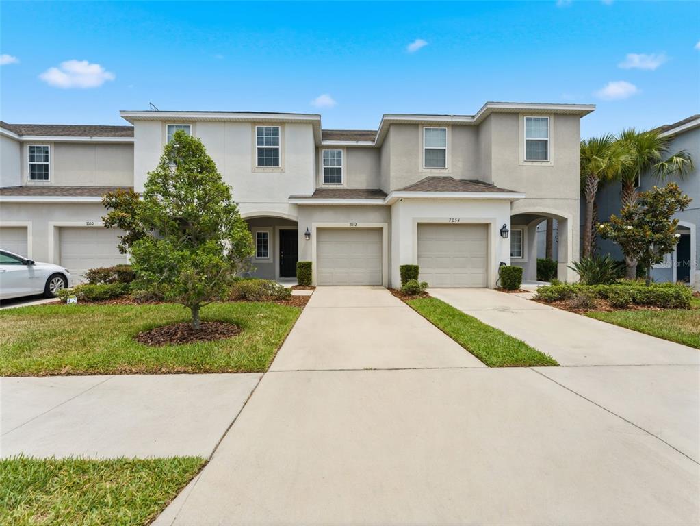 A row of two-story townhouses with beige stucco siding, attached garages, and concrete driveways — 7052 GRAND ELM DRIVE, RIVERVIEW, FL
