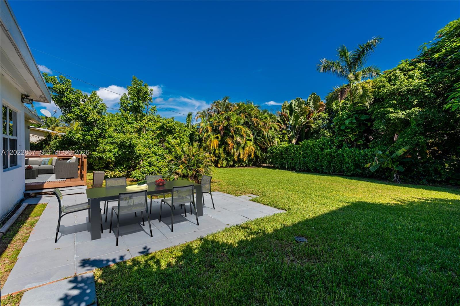 A patio with a dining set sits in a backyard surrounded by lush green trees — 66 NW 87th St, El Portal FL 33150, EL PORTAL, FL
