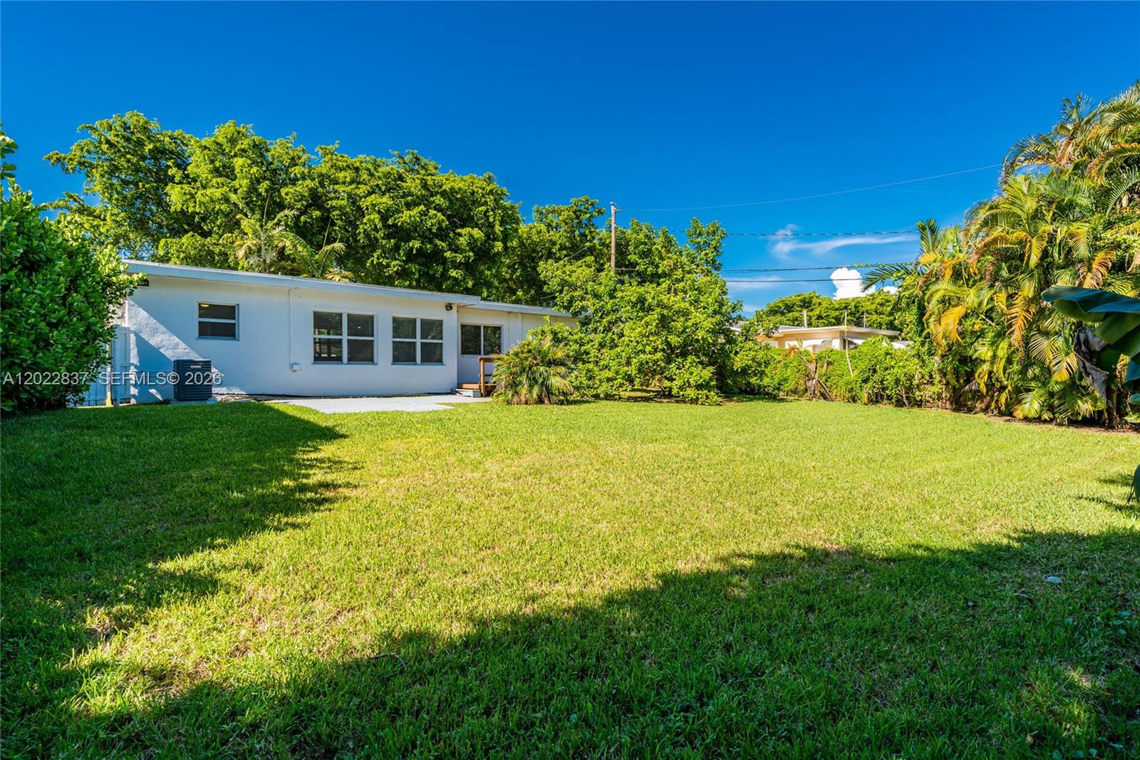 The backyard features a white house with a concrete patio and lush green landscaping — 66 NW 87th St, El Portal FL 33150, EL PORTAL, FL