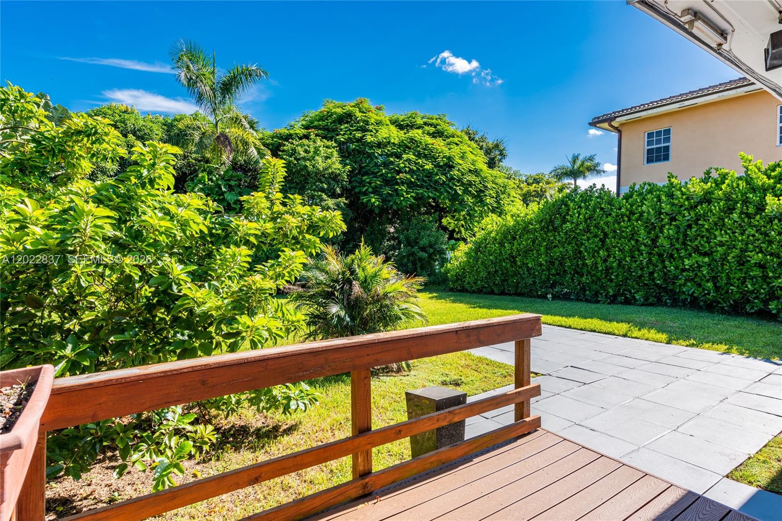 A wooden deck overlooks a grassy backyard with a patio and dense green landscaping — 66 NW 87th St, El Portal FL 33150, EL PORTAL, FL