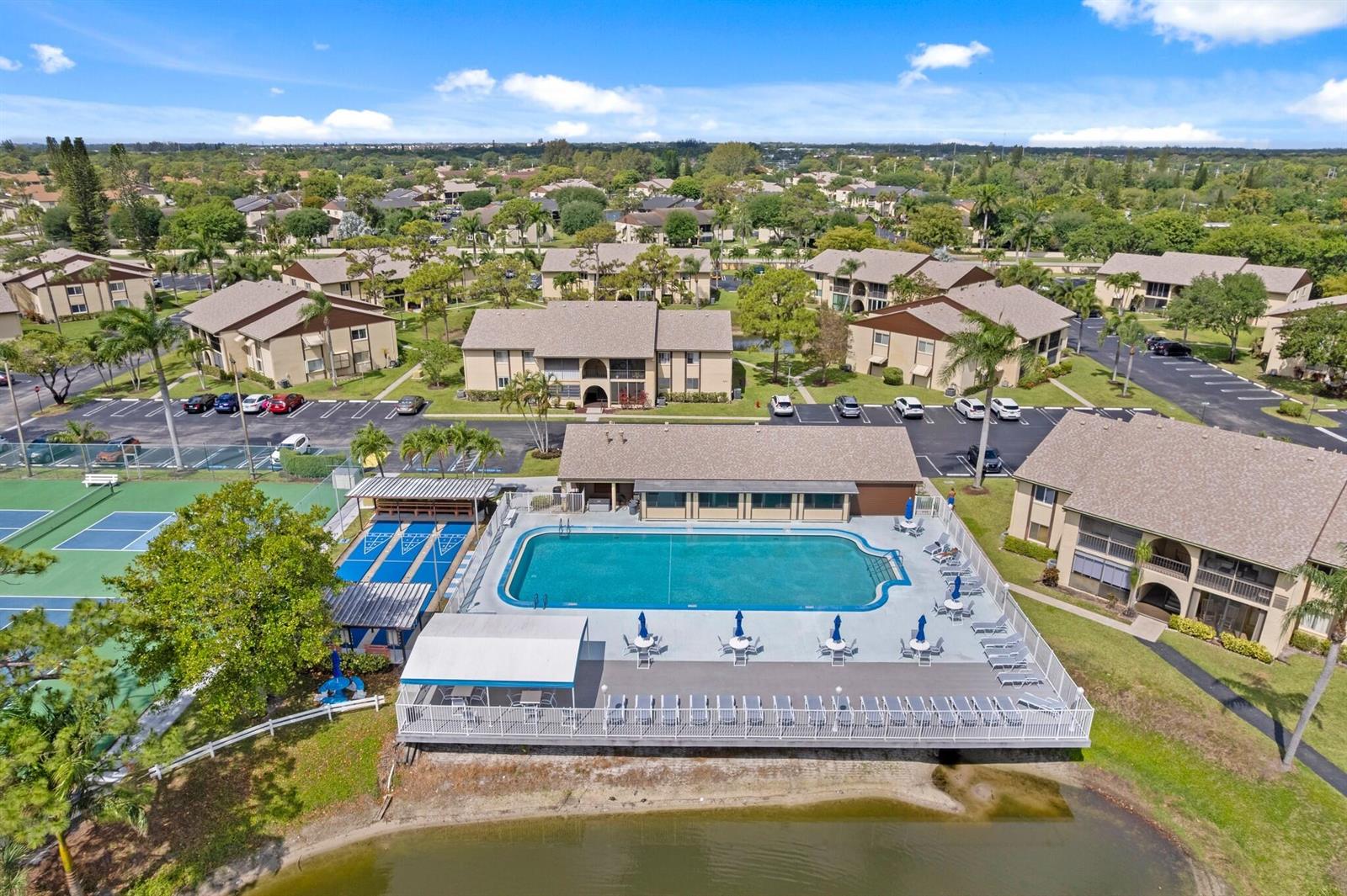 An aerial view shows a swimming pool, tennis courts, and apartment buildings near a lake — 337 Pine Ridge Circle # 2, FL 33463, FL