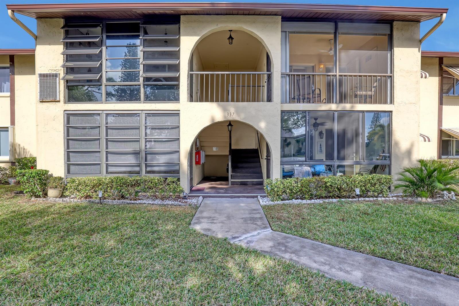 A two-story apartment building exterior features arched entryways, screened balconies, and a concrete walkway — 337 Pine Ridge Circle # 2, FL 33463, FL