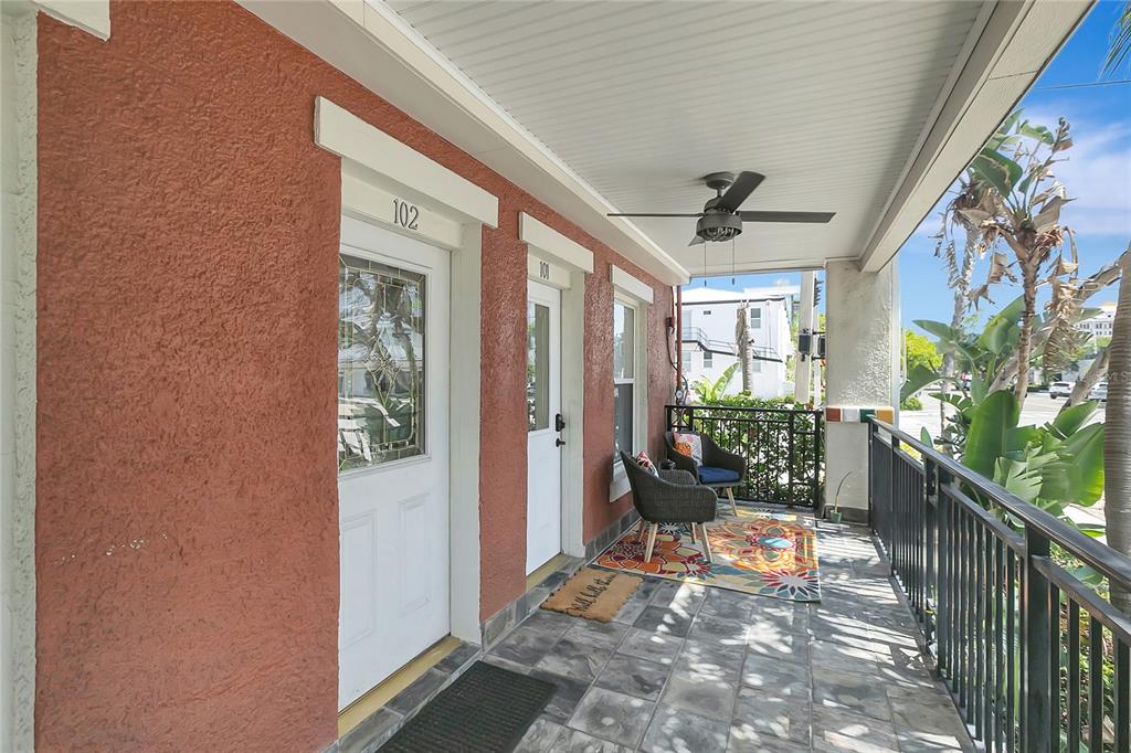 A covered porch features tiled flooring, two chairs, a ceiling fan, and two unit doors — 201 6TH STREET S UNIT 102, ST PETERSBURG, FL