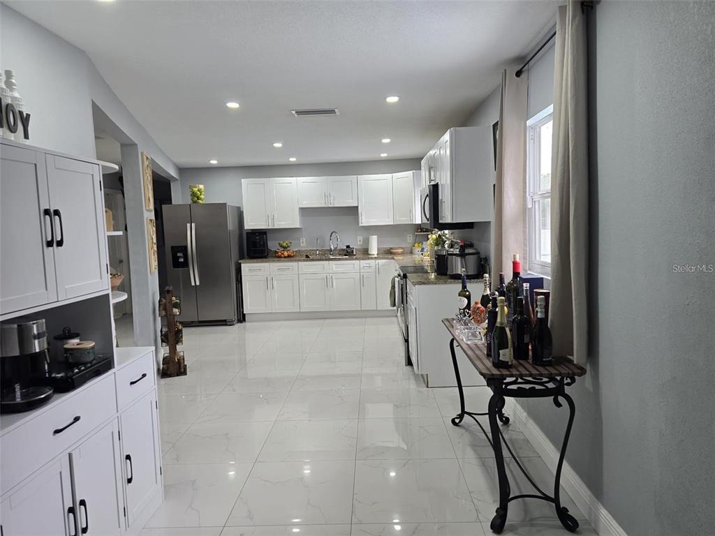 A white kitchen features stainless steel appliances, tile flooring, and a console table with bottles — 16225 WHIPPOORWILL LANE, SPRING HILL, FL