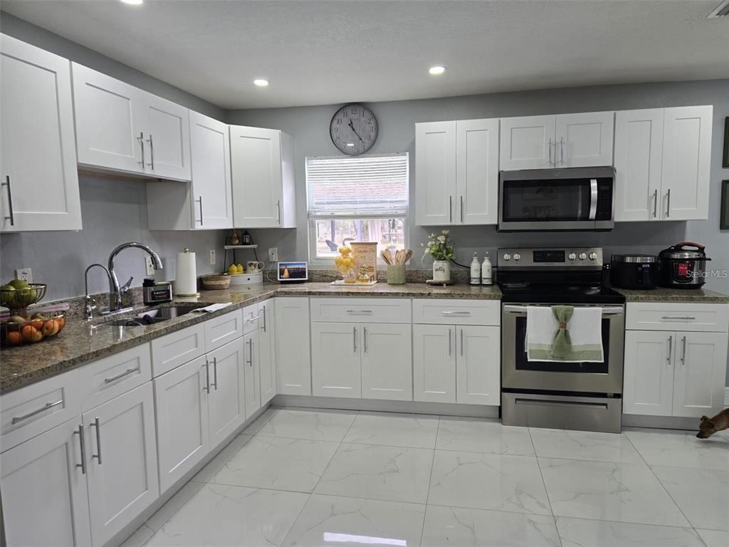 A kitchen features white cabinets, stainless steel appliances, granite countertops, and light-colored tile flooring — 16225 WHIPPOORWILL LANE, SPRING HILL, FL